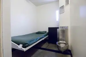 Empty jail cell showing cot, sink, toilet.